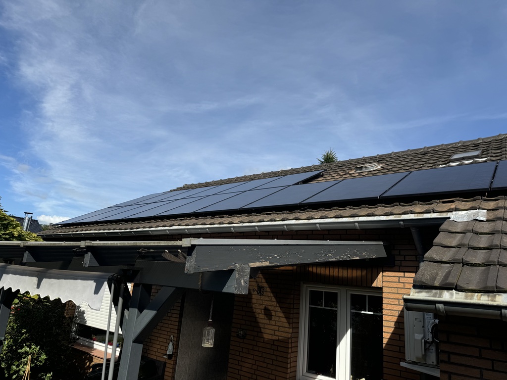 Ziegeldach eines Hauses mit installierten Solarpanels unter blauem Himmel. Holzdach vorn.
