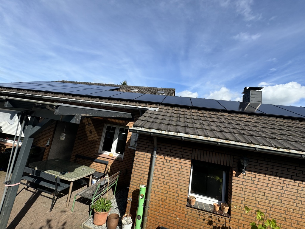 Backstein-Gebäude mit Solarpaneelen, klarer Himmel, Tisch und Pflanzen auf der Terrasse.