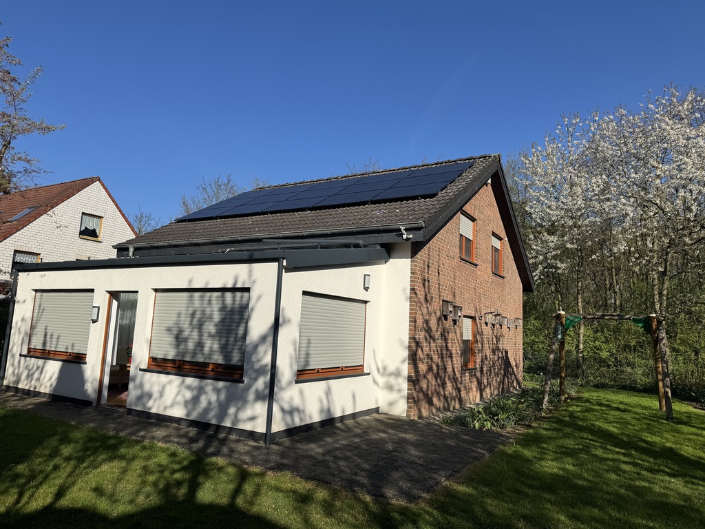 Ein modernes Haus mit Solarpanelen, rotem Ziegel und weißer Fassade vor blauem Himmel.