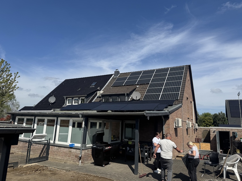 Zwei Personen diskutieren neben einem Haus mit Solarpaneelen unter klarem Himmel.
