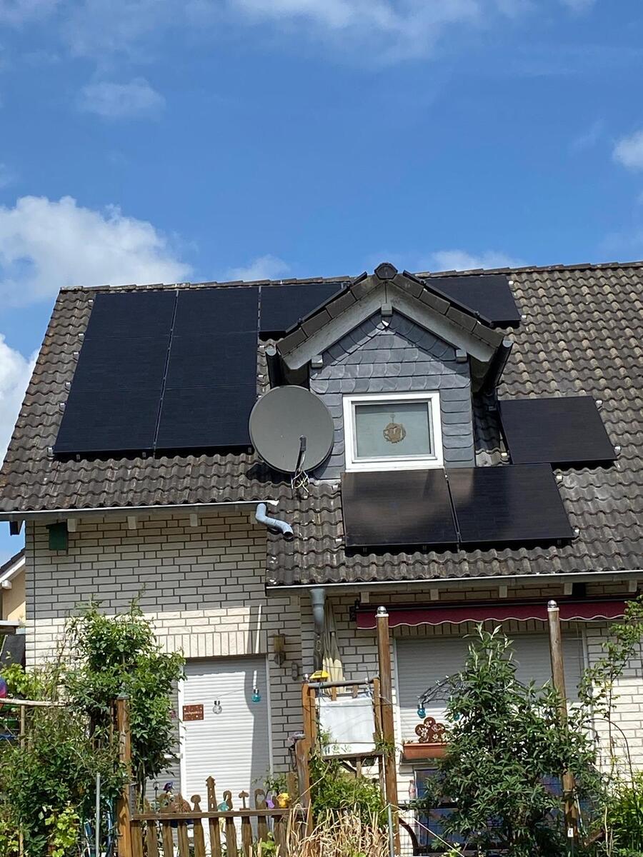 Dach eines Hauses mit Solarpanelen und Satellitenschüssel, blauer Himmel und grüne Pflanzen.