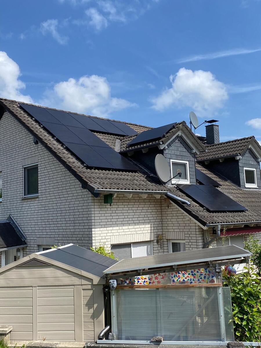 Ein Haus mit schwarzen Solarmodulen auf dem Dach unter blauem Himmel und weißen Wolken.