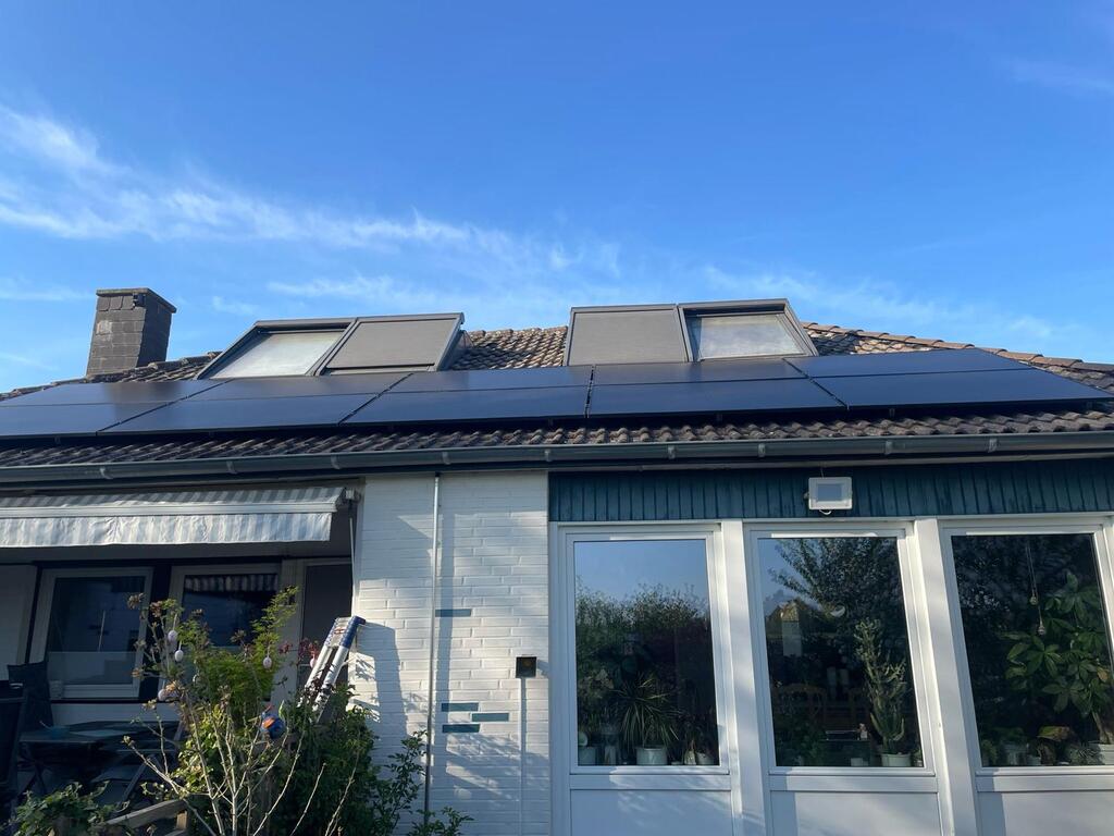 Ein Hausdach mit Solarpaneelen, mehrere Dachfenster, klare blauer Himmel, modernes Design.
