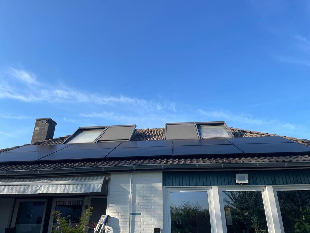 Hausdach mit Solarpanelen, blauer Himmel, weiße Wände, große Fenster, schlichte moderne Architektur.
