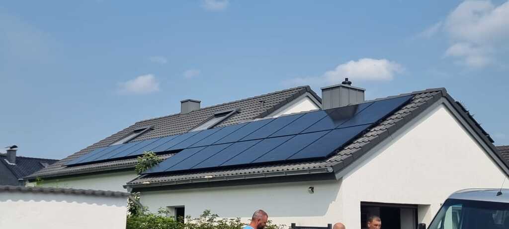 Einfamilienhaus mit Solarpanelen auf dem Dach; drei Personen im Vordergrund, sonniger Tag.