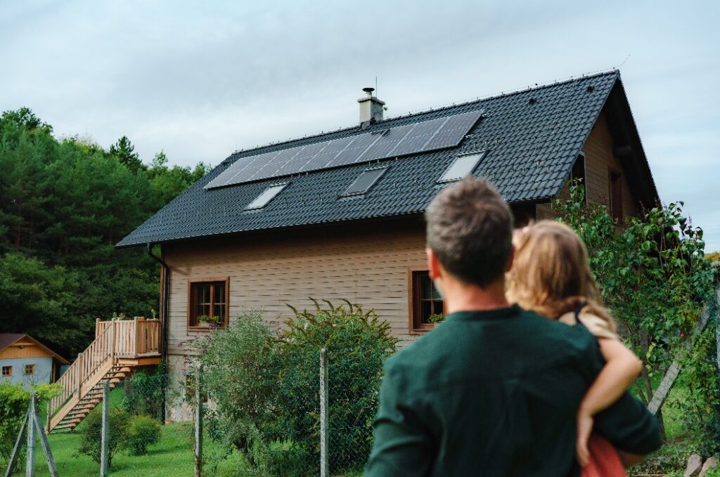Vater mit Tochter vor Haus mit Solarpanels.